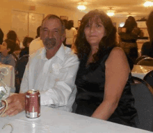 a man and a woman are sitting at a table with a can of soda on it .