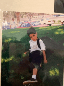 a young boy with a backpack sits on a skateboard in the grass