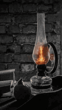 a black and white photo of an old oil lamp sitting on a table next to a brick wall .