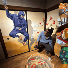 a man kneeling in front of a painting of a ninja and a fish tank