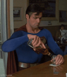a man dressed as superman is pouring a drink into a glass