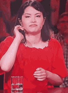 a woman in a red shirt is sitting at a table with a glass of water in front of her .