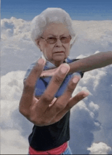 an elderly woman wearing glasses and a black shirt is giving a middle finger while standing in the clouds