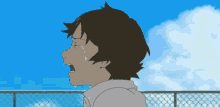 a boy is crying in front of a chain link fence and a blue sky .