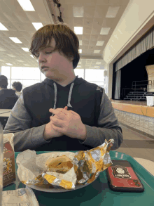 a boy is sitting at a table with a plate of food and a cell phone that says galaxy