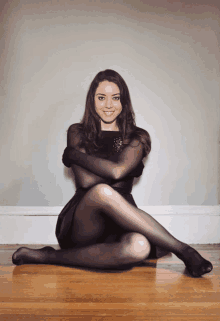 a woman in a black dress and tights sits on the floor with her legs crossed