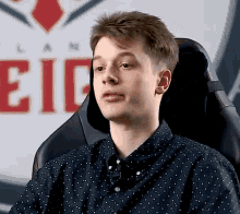 a young man in a polka dot shirt is sitting in a chair in front of a sign that says eic