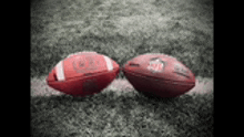 two red footballs are sitting on top of a field .