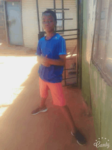 a boy in a blue shirt and orange shorts is standing in front of a building with the word candy on the bottom