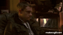 a man in a leather jacket and tie is sitting in a chair with his face covered .