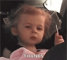 a little girl is holding a lollipop and saying `` thanks '' .