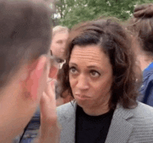 a woman in a suit is making a funny face while talking to a man in a crowd .