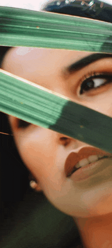 a close up of a woman 's face with a green leaf covering half of her face