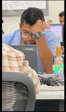 a man sitting at a desk with his head resting on his hand while wearing glasses