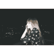 a woman wearing a black shirt with white stars on it looks out over a city at night