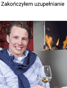 a man in a blue and white striped shirt holds a glass of wine in front of a fireplace