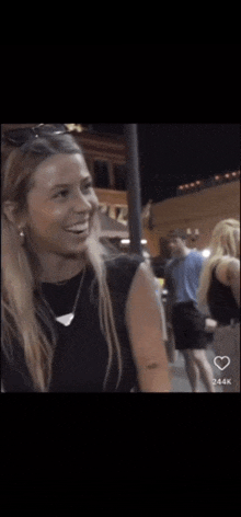 a woman in a black shirt is smiling while walking down a street at night