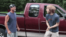 two men are standing next to a red truck and one of them is wearing a shirt that says ' i love you ' on it