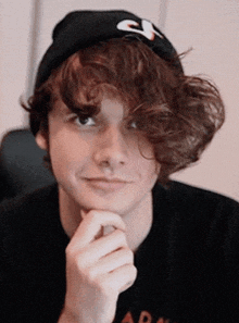 a young man with curly hair wearing a black hat and a black shirt with the word ada on it