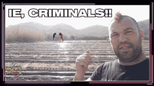 a man with a mohawk stands in front of a sign that says ' ie criminals ' on it