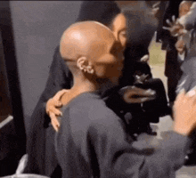 a bald man is being hugged by a woman in a crowd .