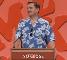 a man in a blue shirt is standing at a podium with the words `` so close '' written on the podium .