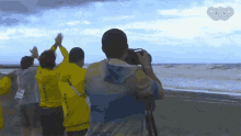 a man taking a picture of a group of people on a beach with the olympics logo in the background