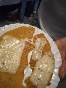 a person is holding a paper plate with a piece of food on it that has cheese on it