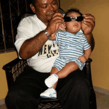 a man is holding a baby wearing sunglasses while sitting on a chair .