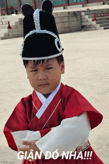 a young boy wearing a black hat and a red kimono is standing in front of a sign that says gian do nha !!!