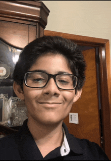 a boy wearing glasses and a black shirt smiles