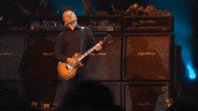 a man is playing a guitar in front of a wall of amps that say highland & keithman