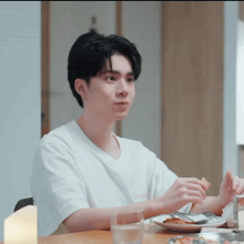 a young man sitting at a table with a plate of food in front of him