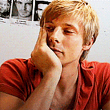 a young man in a red shirt holds his hand to his face