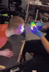a person wearing blue gloves holds a rainbow colored object in front of a child 's face