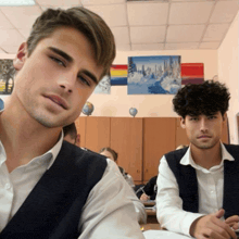 two men are sitting in a classroom with a painting on the wall