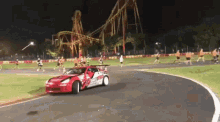 a red and white race car is driving on a track at night with a roller coaster in the background