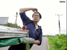 a man with glasses and a backpack is standing next to a trash can on the side of a road .