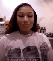 a woman wearing a white t-shirt with a picture of two cans on it is talking to someone in a kitchen .