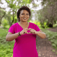 a woman in a pink shirt is making a heart with her hands