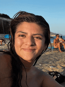 a woman taking a selfie on the beach with a man sitting in the background