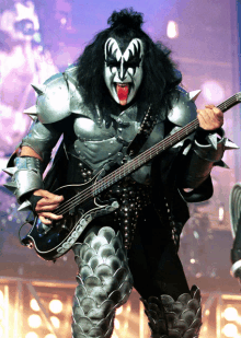 a man wearing a mask and armor is playing a bass guitar