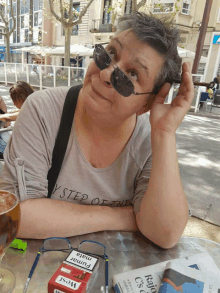 a woman wearing sunglasses sits at a table with a pack of west cigarettes