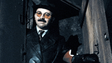 a man wearing a hat and sunglasses stands in a dark room