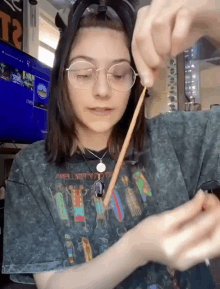 a girl wearing glasses and a t-shirt that says t2 is holding a stick in her hand