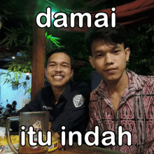 two young men sitting next to each other with a mug that says itu indah on it