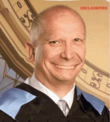 a man in a graduation cap and gown is smiling with the words declassified behind him