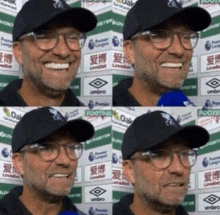 a man wearing glasses and a hat is smiling in front of a sign that says umbro