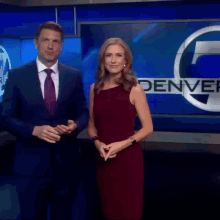 a man in a suit and tie and a woman in a red dress stand in front of a denver sign