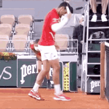 a man in a red shirt and white shorts is standing on a tennis court holding a tennis racket .